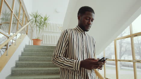 Hombre-Afroamericano-Parado-En-La-Escalera-Y-Usando-Un-Teléfono-Inteligente